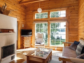 A cozy cabin interior with a fireplace, television, comfortable seating, and large windows offering a view of the outdoors.