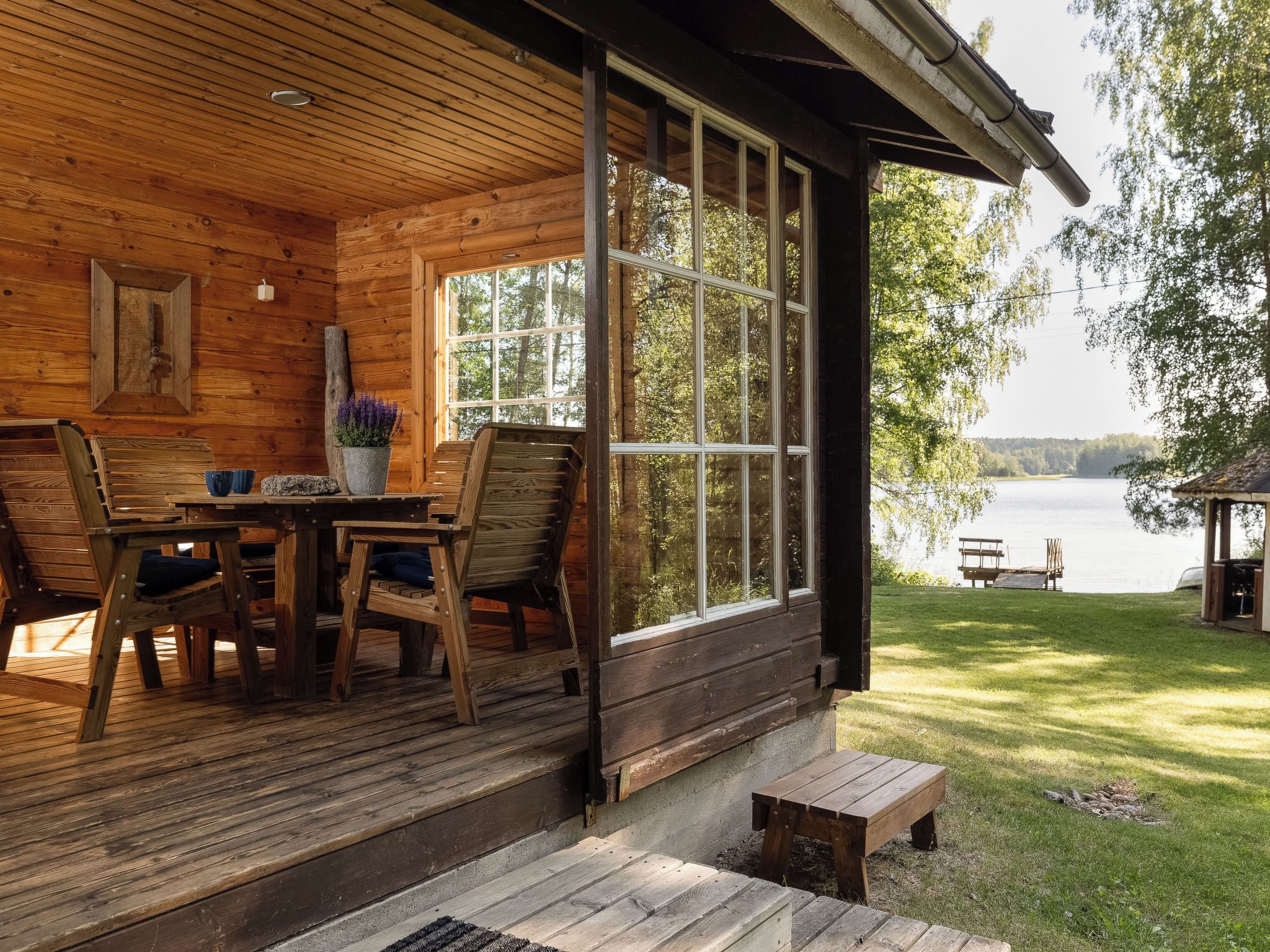 A wooden cabin with a porch, a table, chairs, and a view of a lake.