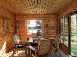 A wooden cabin interior with a dining table, chairs, a window with a view of trees, and a decorative wall piece.