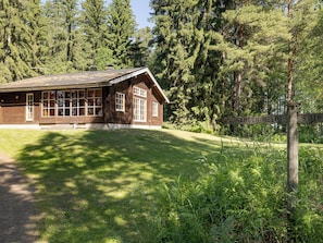 A wooden cabin with large windows, surrounded by dense forest.