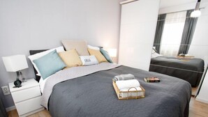 A modern bedroom with a large bed, a smaller bed, a bedside table with a lamp, and a bedside basket. - Gezeiten by Interhome (Norddeich)