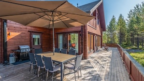 Een houten terras met een tafel, stoelen, een barbecue en een grote parasol voor schaduw.