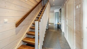 Een houten trap met een leuning, leidend naar een gang met een deur en een bankje.