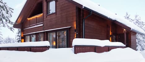 A wooden cabin with a large balcony, surrounded by snow.
