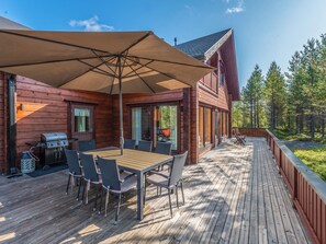 A wooden deck with a table and chairs, a barbecue grill, and a large umbrella.