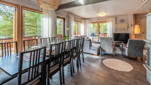Een ruime eetruimte met een hoge plafond, grote ramen en een moderne kroonluchter.