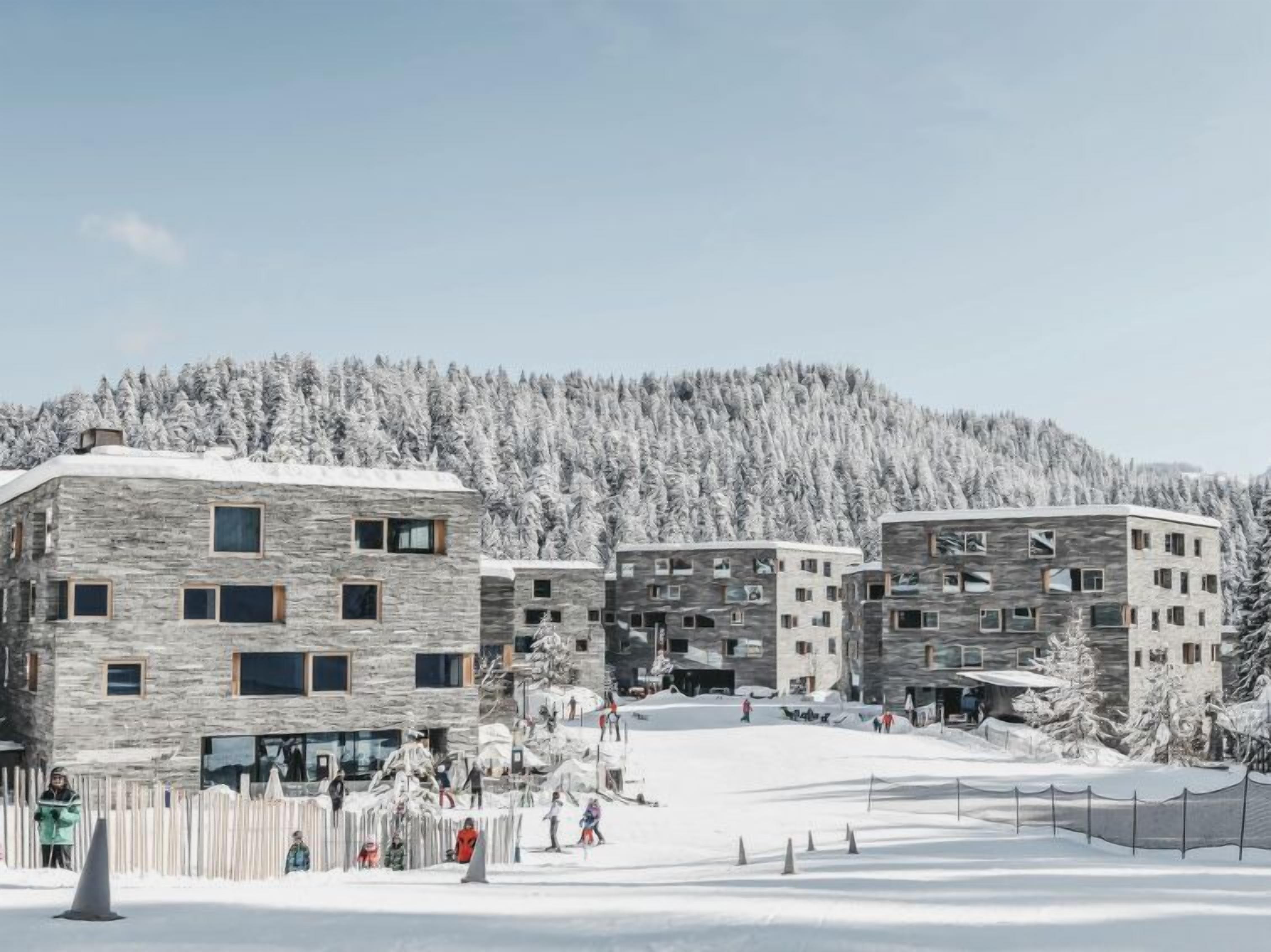 Ein moderner Gebäudekomplex mit mehreren Stockwerken und großen Fenstern, umgeben von schneebedeckten Bäumen und blauem Himmel.