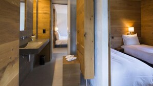 A modern hotel room with wooden walls, a wooden bed, a bedside table, a nightstand, a mirror, and a bathroom with a sink and toilet. - Superior Alpine by Interhome (Laax)