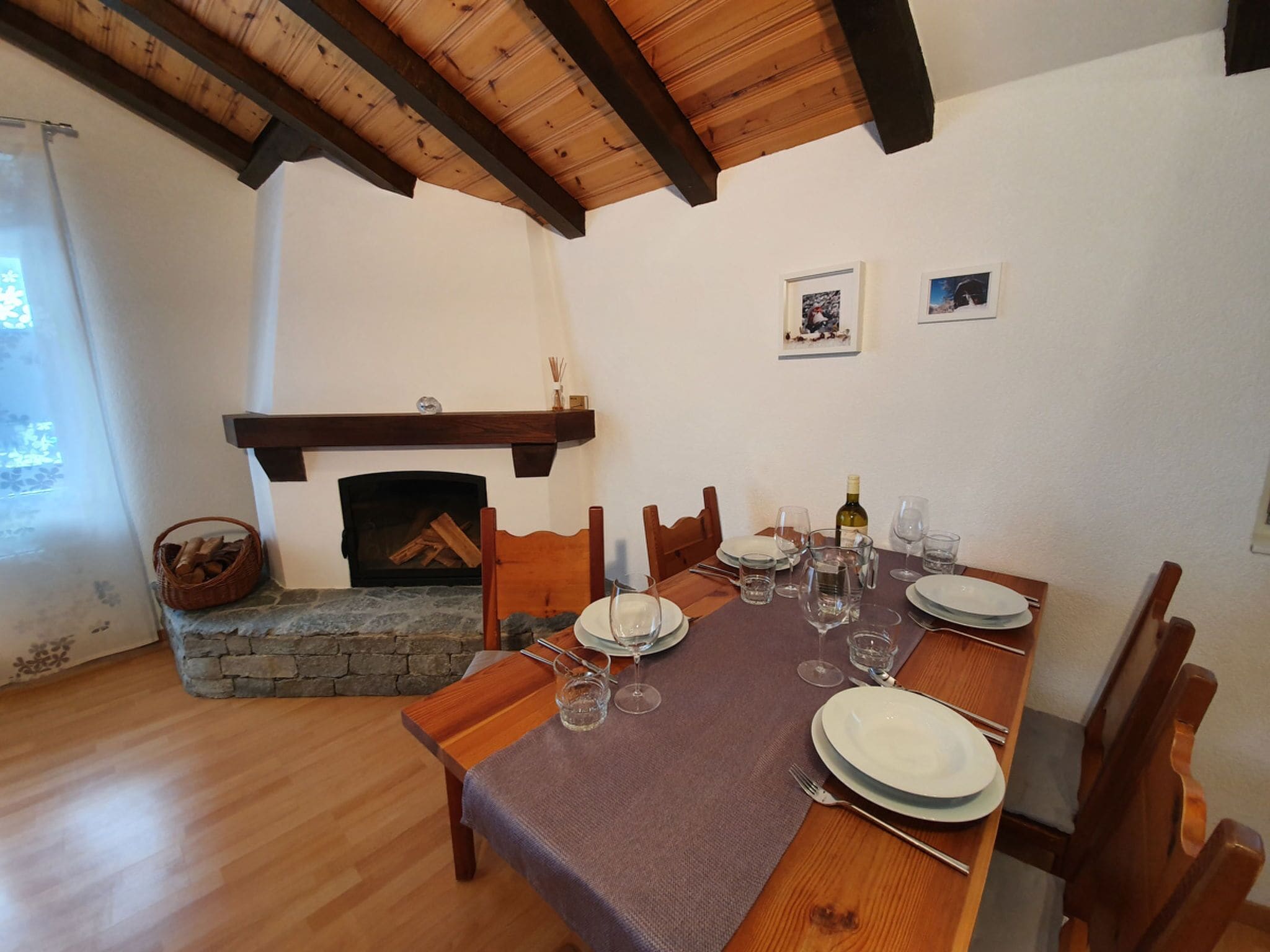 Un coin repas avec une table en bois dressée pour quatre personnes, une cheminée en pierre et un plafond en bois.