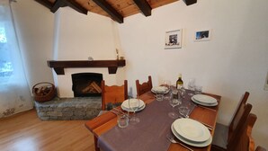 Uma sala de jantar com mesa de madeira posta para quatro pessoas, lareira de pedra e teto de madeira.