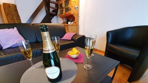 Uma garrafa de champanhe La Cuvee sobre uma mesa, com dois copos de champanhe, uma tigela de limões e um guardanapo rosa.