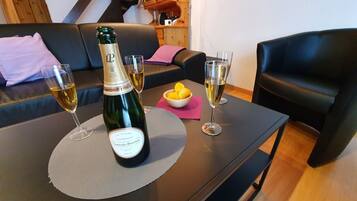 Une bouteille de champagne La Cuvée est posée sur une table, accompagnée de deux verres à champagne, d’un bol de citrons et d’une serviette rose.