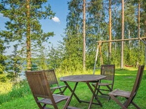 An outdoor seating area with a table and chairs, surrounded by trees and a view of a body of water.