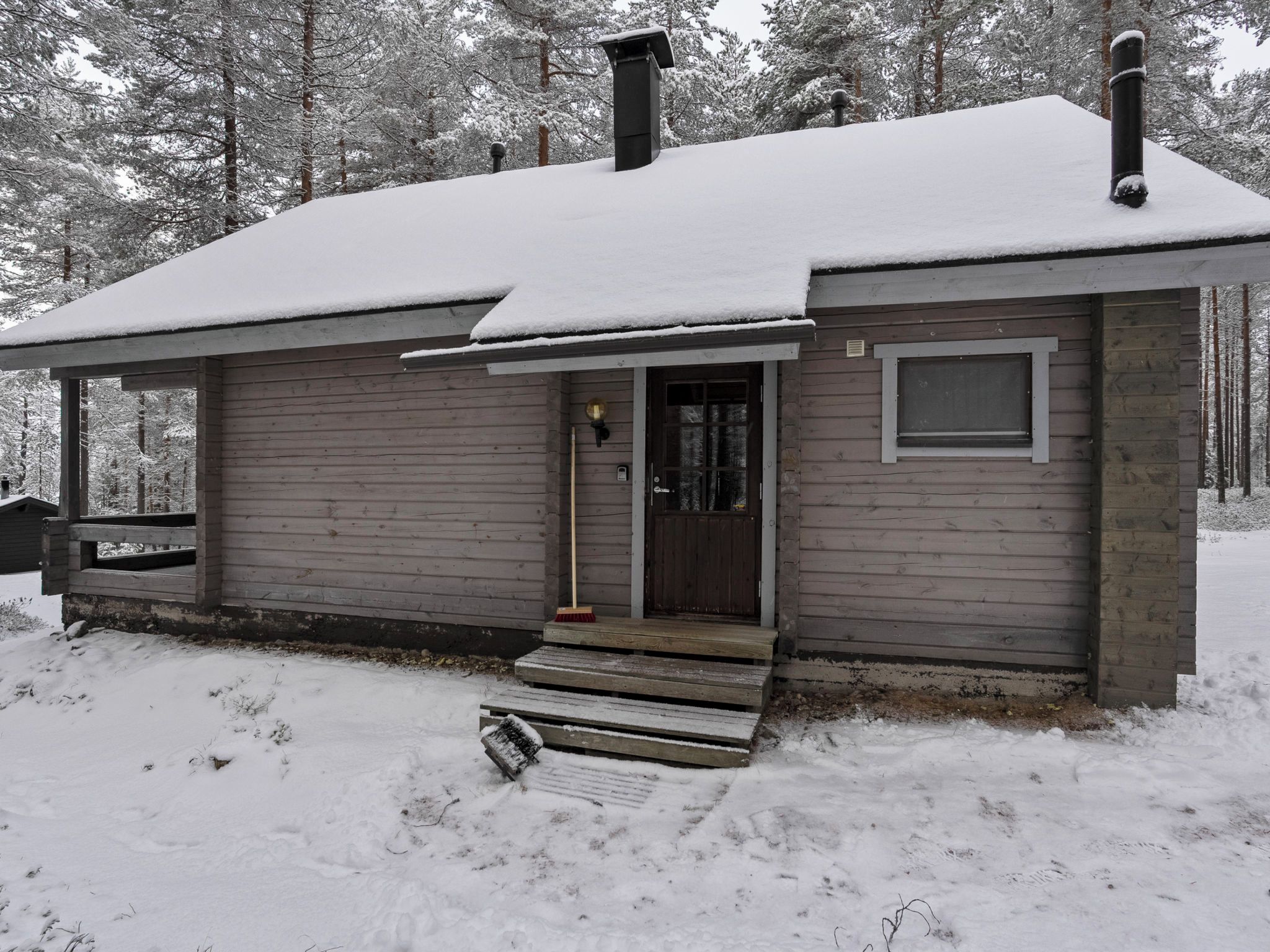 Una cabaña de madera con techo nevado, una puerta principal y un pequeño porche.