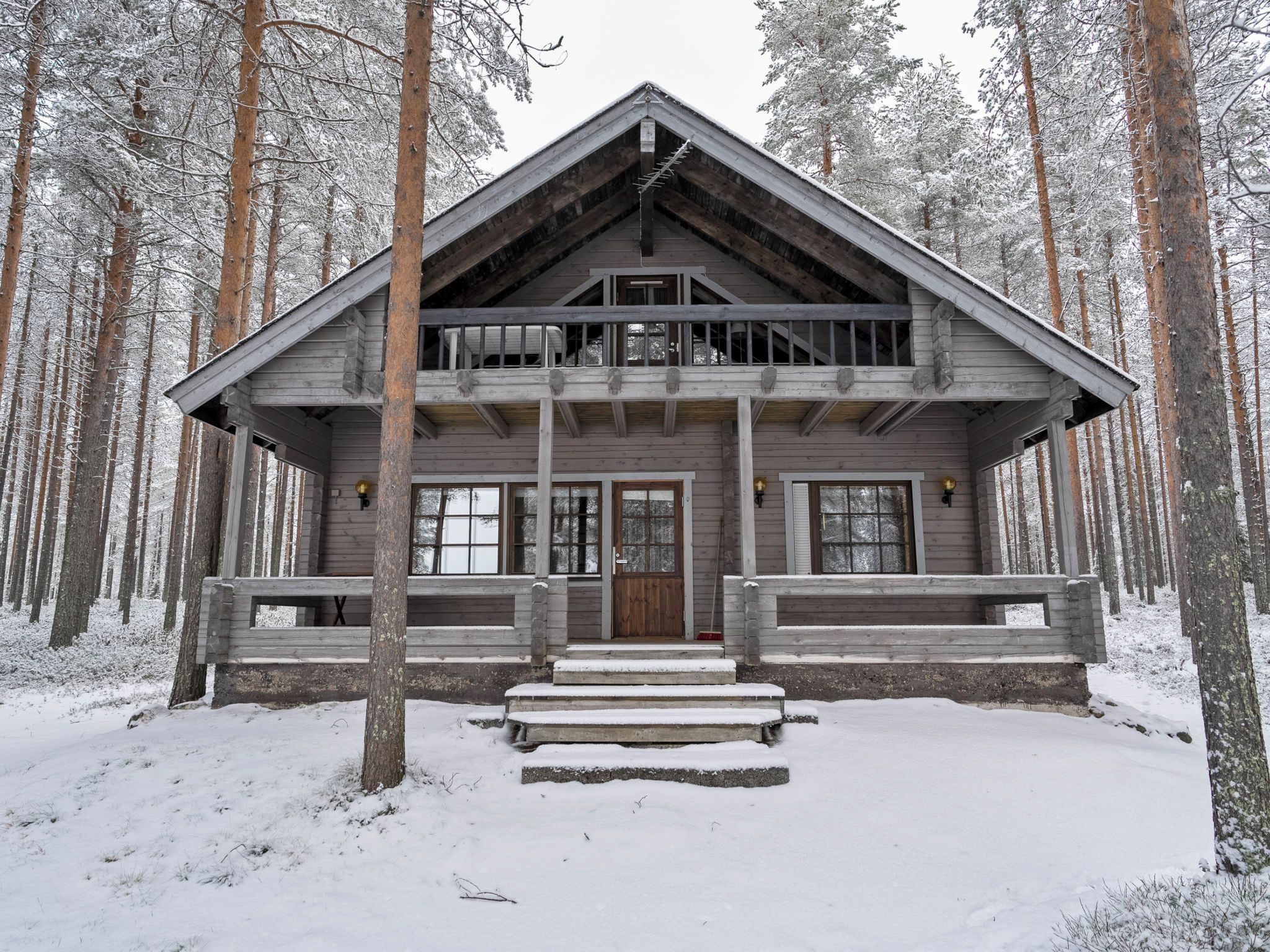 Uma cabana de madeira com varanda, rodeada por árvores cobertas de neve.
