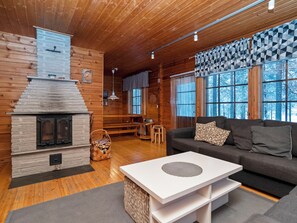 A cozy cabin interior with a fireplace, wooden walls, a sofa, and a dining area. - Kitkaranta by Interhome (Kuusamo)