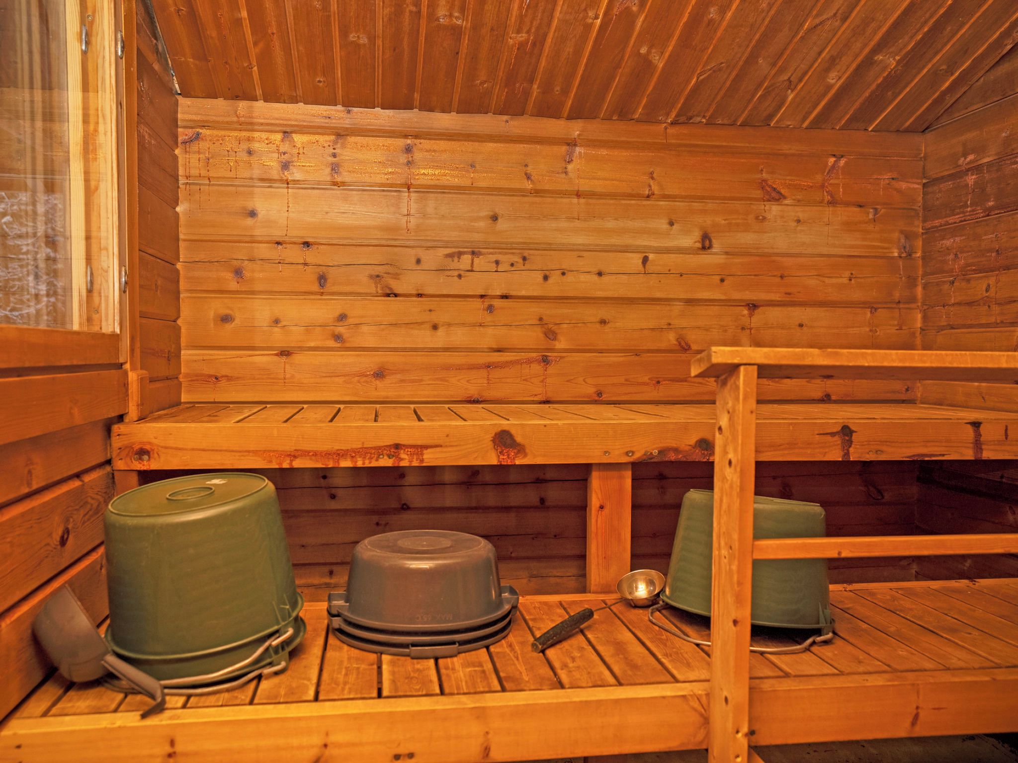 L’intérieur d’une cabane en bois, avec un lit superposé, une petite table et un récipient vert.