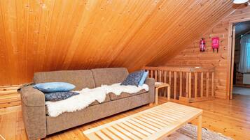 Een knus loft slaapkamer met een schuine plafond, houten wanden, een bank, een kleine tafel en een bed.