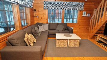 Interior acogedor de una cabaña con un sofá seccional, una mesa de centro y ventanas amplias que ofrecen vistas a un bosque nevado.