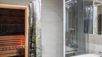 A modern bathroom with a glass shower enclosure, a wooden sauna area, and a white sink.