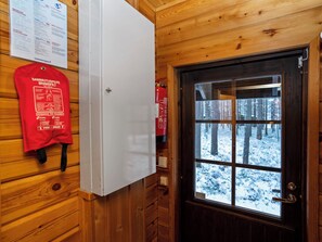 A wooden cabin interior with a white refrigerator, a fire extinguisher, and a door leading to a snowy forest view. - Kitkaranta by Interhome (Kuusamo)