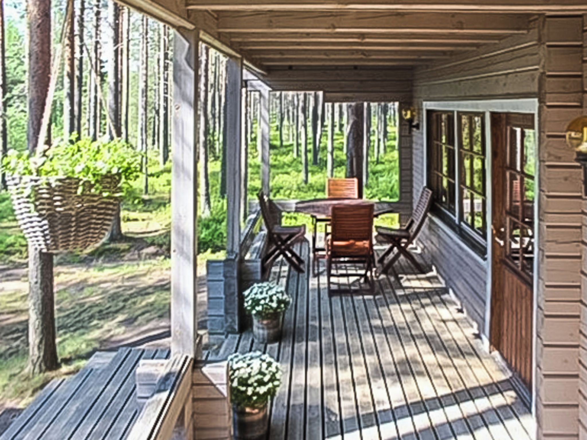 Eine Holzterrasse mit Tisch und Stühlen, umgeben von Fenstern und Blick auf einen Wald.