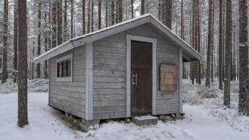 A small wooden cabin with a door and a window, surrounded by snow-covered trees.
