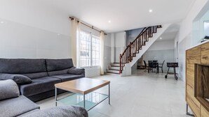 Ein modernes Wohnzimmer mit einem grauen Sofa, einem Glastisch und einer Treppe, die in einen Essbereich führt.