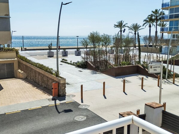Eine Küstenstraße mit freiem Blick auf das Meer, Palmen und einem Gebäude mit der Aufschrift 'Carrer Del Sol'.