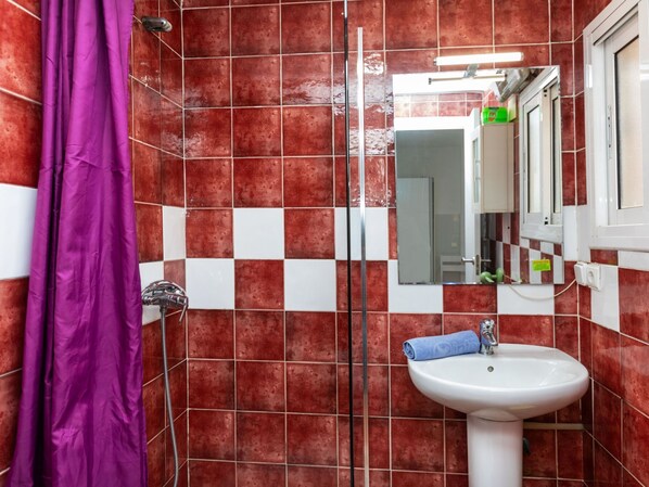 A bathroom with red and white checkered tiles, a purple shower curtain, a white sink with a blue towel, and a mirror with a green sign. - Del Sol by Interhome (Salou)