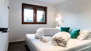 Un dormitorio con cama, almohadas, una lámpara y ventana con vistas a montañas.