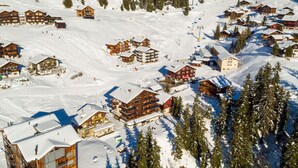 Un pueblo en la montaña cubierto de nieve con edificios de madera, pistas de esquí y un telesilla.