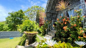 A traditional house with a wooden staircase leading to a porch, surrounded by lush greenery and flowering plants. - Hotra Hill Cottage (Penida Island)