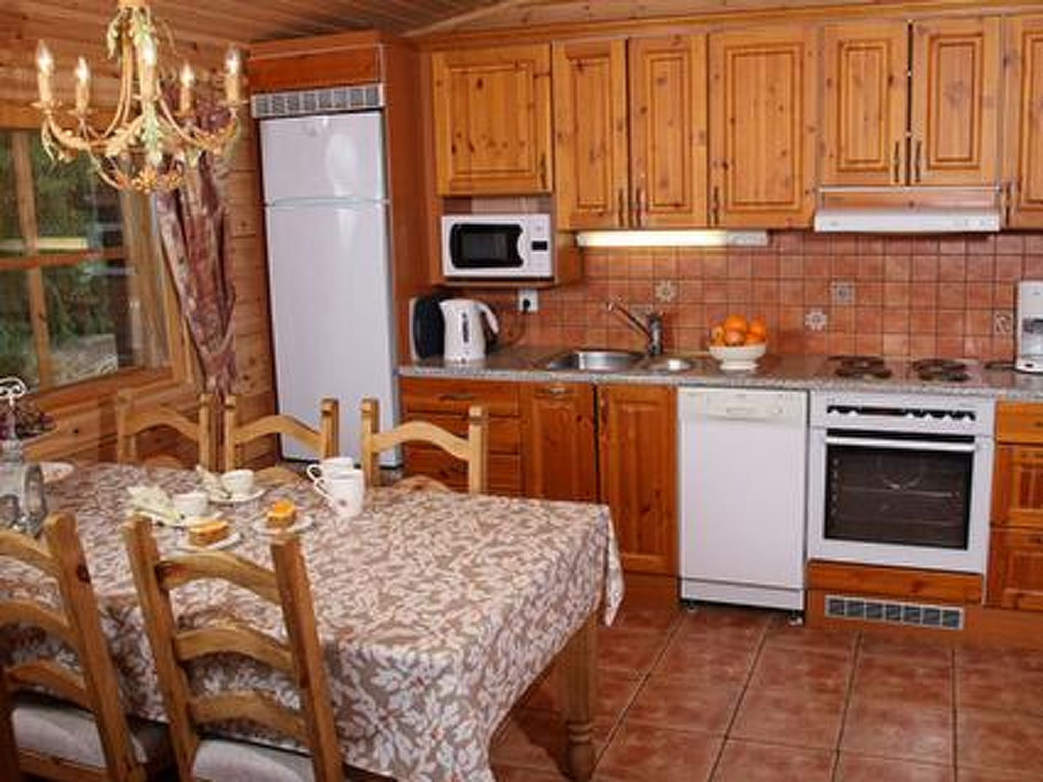 Cuina amb armaris de fusta, nevera, microones, forn i una taula de dinar amb cadires.