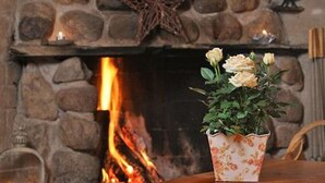 A stone fireplace with a lit fire, a decorative star, and a floral vase with flowers on a wooden table. - Kultaranta by Interhome (Asikkala)