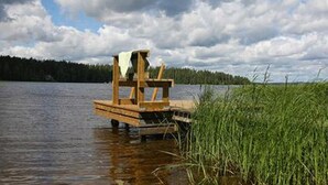 A wooden dock extending into a lake, surrounded by tall grass and a forested shoreline. - Kultaranta by Interhome (Asikkala)