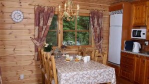 A wooden interior with a dining table set for four, a kitchen with wooden cabinets, and a window with curtains. - Kultaranta by Interhome (Asikkala)