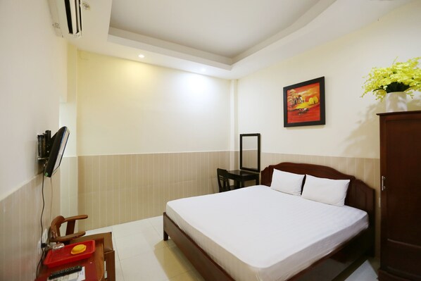A hotel room with a bed, a desk with a chair, a TV, and a painting on the wall. - Minh Quang Hotel (Da Nang)