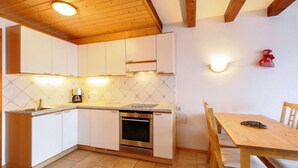 A compact kitchen with white cabinets, a built-in oven, a sink, and a dining area with a wooden table and chairs. - Ermitage 13 by Interhome (Villars)