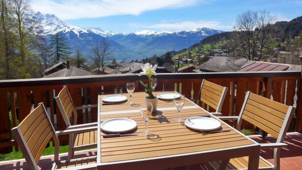 A wooden table set for four with a mountain view, surrounded by wooden chairs. - Ermitage 13 by Interhome (Villars)
