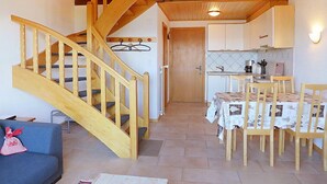 A cozy living room with a wooden staircase, a dining area with a table and chairs, and a kitchen with cabinets and a countertop. - Ermitage 13 by Interhome (Villars)
