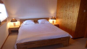 A neatly made bed with white linens in a room with wooden paneling on one wall and a window on the other. There are two bedside tables with lamps. - Ermitage 13 by Interhome (Villars)