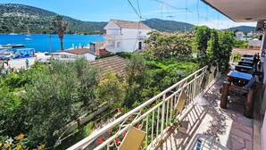 Un balcón con vistas a un pueblo costero, un puerto deportivo con barcos y abundante vegetación.