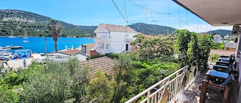 A balcony with a view of a coastal town, a marina with boats, and lush greenery.