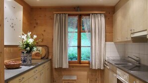 A compact kitchen with wooden cabinets, a built-in oven, a sink, and a window with curtains. - Chalet Maru by Interhome (Lenk)