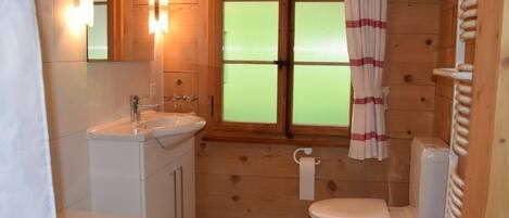 Un baño rústico en una cabaña de madera, con bañera, inodoro y lavamanos.