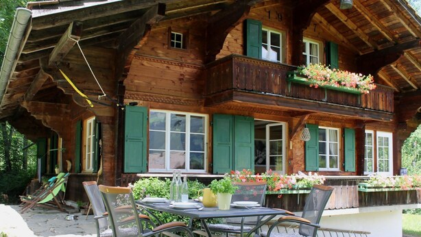 A wooden chalet with a balcony, outdoor seating, and a pond. - Chalet Maru by Interhome (Lenk)