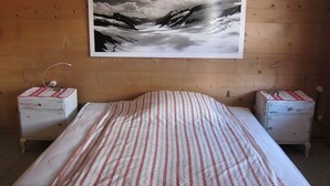A bedroom with a bed, two bedside tables, and a large landscape painting on the wall. - Chalet Maru by Interhome (Lenk)
