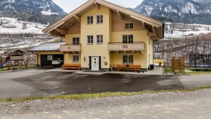Un immeuble à plusieurs étages, doté d’un toit en pente, de balcons et d’un espace de stationnement, situé dans une région montagneuse.