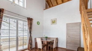 Une pièce avec un plancher en bois, une table à manger avec des chaises, une porte-fenêtre coulissante, un escalier et une porte.